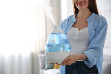 Woman with modern air humidifier at home, closeup. Space for text