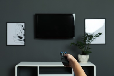 Woman switching channels on plasma TV with remote control at home
