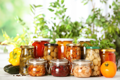 Glass jars of different pickled vegetables on white wooden table