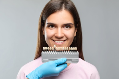 Doctor checking young woman's teeth color on light grey background. Cosmetic dentistry