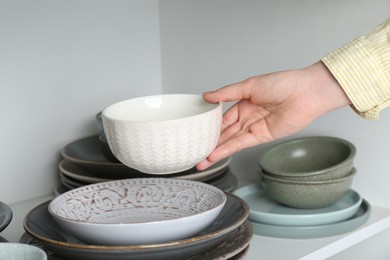 Woman taking ceramic bowl from shelf, closeup