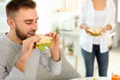 Photo of Young man having breakfast with sandwiches in kitchen, space for text