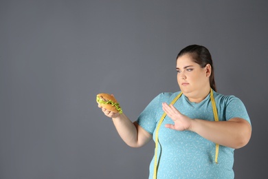 Photo of Overweight woman with hamburger and measuring tape on gray background. Space for text