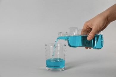 Woman pouring mouthwash into glass on light grey background, closeup