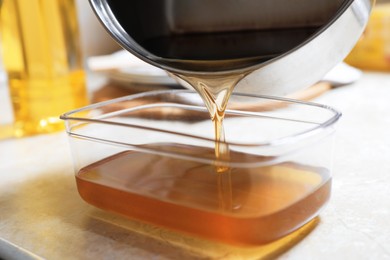Photo of Pouring used cooking oil from saucepan into container on beige table, closeup