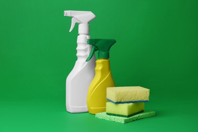 Photo of Spray bottles of detergents and sponges on green background. Cleaning supplies