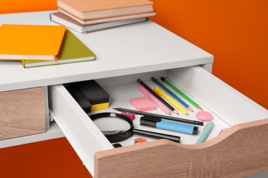 Photo of Office supplies in open desk drawer on orange background
