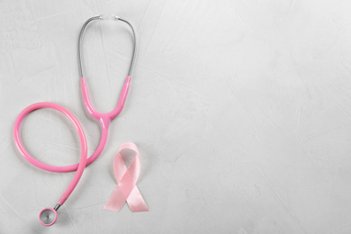 Pink ribbon and stethoscope on light grey stone background, flat lay with space for text. Breast cancer concept