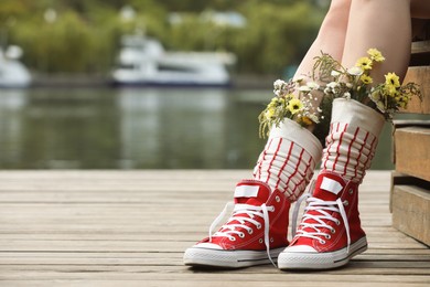 Woman sitting on wooden pier with flowers in socks outdoors, closeup. Space for text