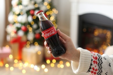 Photo of MYKOLAIV, UKRAINE - JANUARY 18, 2021: Woman holding Coca-Cola bottle in room decorated for Christmas, closeup