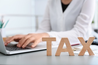 Word TAX an blurred woman with laptop on background