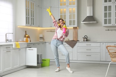 Beautiful young woman with headphones singing while cleaning kitchen
