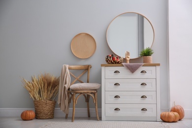 Round mirror and chest of drawers near grey wall in hallway. Interior design