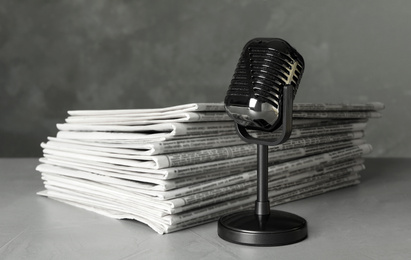 Newspapers and vintage microphone on light grey stone table. Journalist's work
