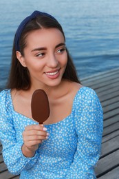 Beautiful young woman eating ice cream glazed in chocolate on pier