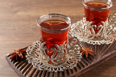 Photo of Glasses of traditional Turkish tea in vintage holders and anise stars on wooden table, closeup