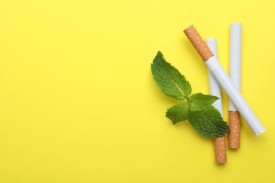Menthol cigarettes and mint on yellow background, flat lay. Space for text