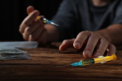 Photo of Addicted man at wooden table, focus on syringe. Hard drugs