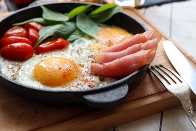 Photo of Delicious fried eggs with spinach, tomatoes and ham served on table, closeup