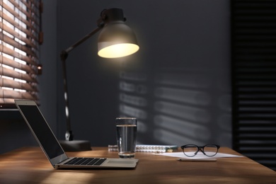 Modern laptop and lamp on table near window in office. Space for text