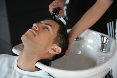 Professional barber washing client's hair at sink in salon, closeup