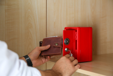 Man putting wallet into small red steel safe, closeup