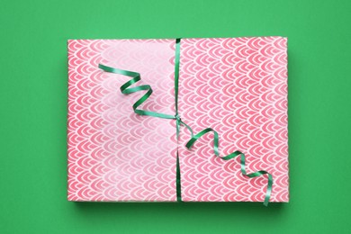 Beautifully wrapped gift box with ribbon on green background, top view