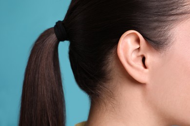 Woman on light blue background, closeup of ear