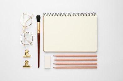 Composition with sketchbook, glasses and stationary on white background, top view