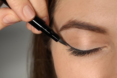 Photo of Artist applying black eyeliner onto woman's face on grey background, closeup