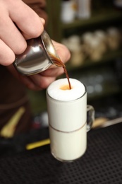 Barista adding coffee to steamed milk at counter, closeup view
