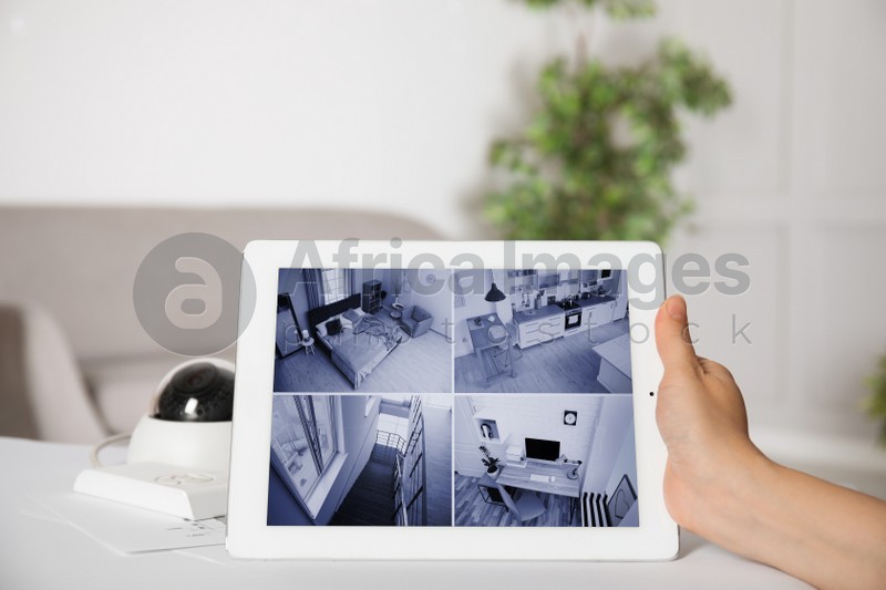 Photo of Woman monitoring CCTV camera on tablet at table indoors, closeup. Home security system