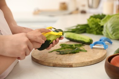 Mother teaching daughter to peel vegetable at kitchen counter, closeup