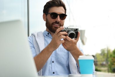 Photo of Man with camera, coffee and laptop in outdoor cafe. Interesting hobby