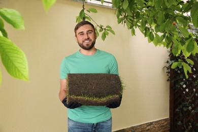 Young man holding rolled grass sod at backyard