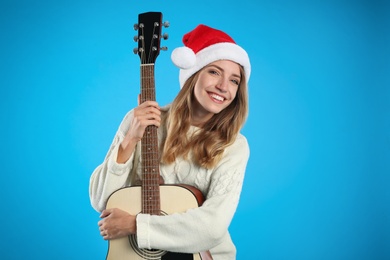 Young woman in Santa hat with acoustic guitar on light blue background. Christmas music