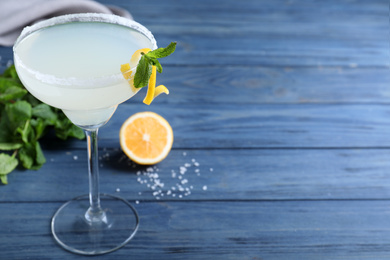 Photo of Glass of tasty Margarita cocktail on blue wooden table. Space for text