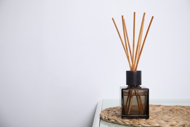 Photo of Aromatic reed freshener on table near white wall, space for text