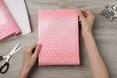 Woman wrapping gift with beautiful paper at wooden table, top view