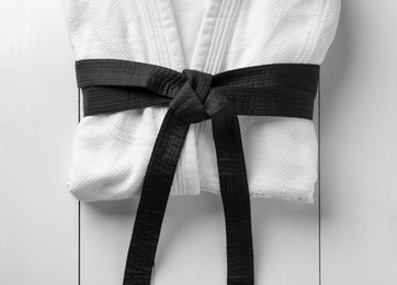 Martial arts uniform with black belt on white wooden background, top view