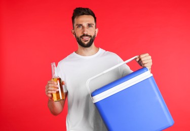 Happy man with cool box and bottle of beer on red background