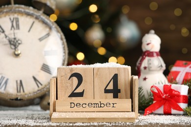 December 24 - Christmas Eve. Wooden block calendar, watch and festive decor on table against blurred lights