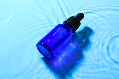 Photo of Bottle of face serum in water on light blue background