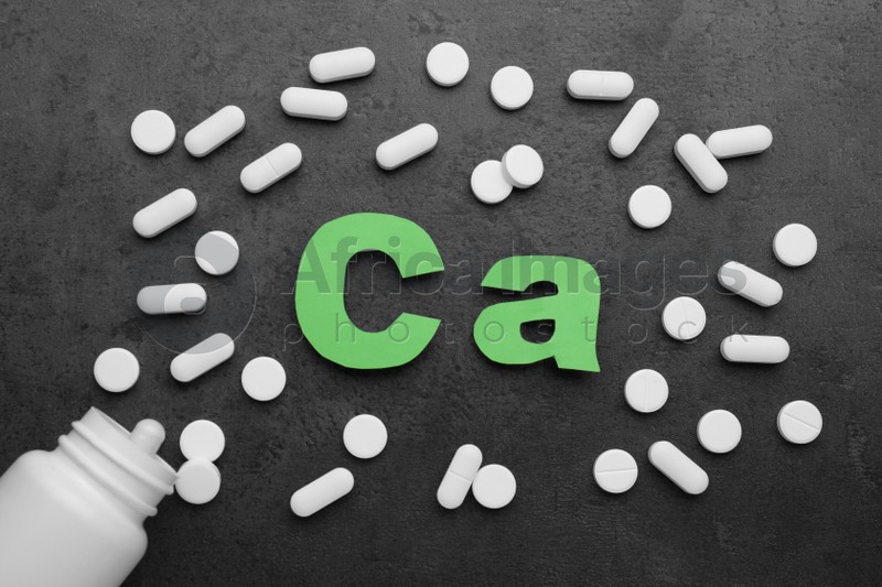 Photo of Paper symbol Ca (Calcium), medical bottle and pills on black background, flat lay