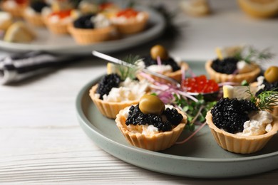 Photo of Delicious tartlets with caviar and cream cheese served on white wooden table, closeup