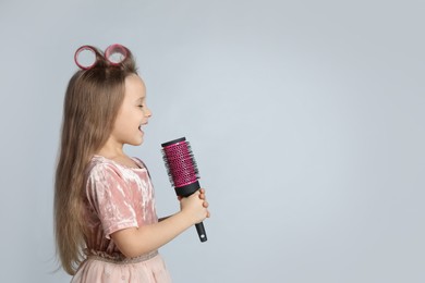 Photo of Cute little girl with hairbrush singing on light grey background, space for text