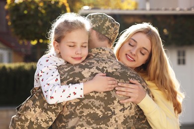 Photo of Daughter and wife hugging soldier in Ukrainian military uniform outdoors. Family reunion