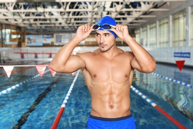 Young athletic man in cap and goggles near swimming pool