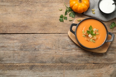 Tasty creamy pumpkin soup with croutons, seeds and parsley in bowl on wooden table, flat lay. Space for text