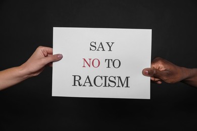 Woman and African American man holding sign with phrase Say No To Racism on black background, closeup